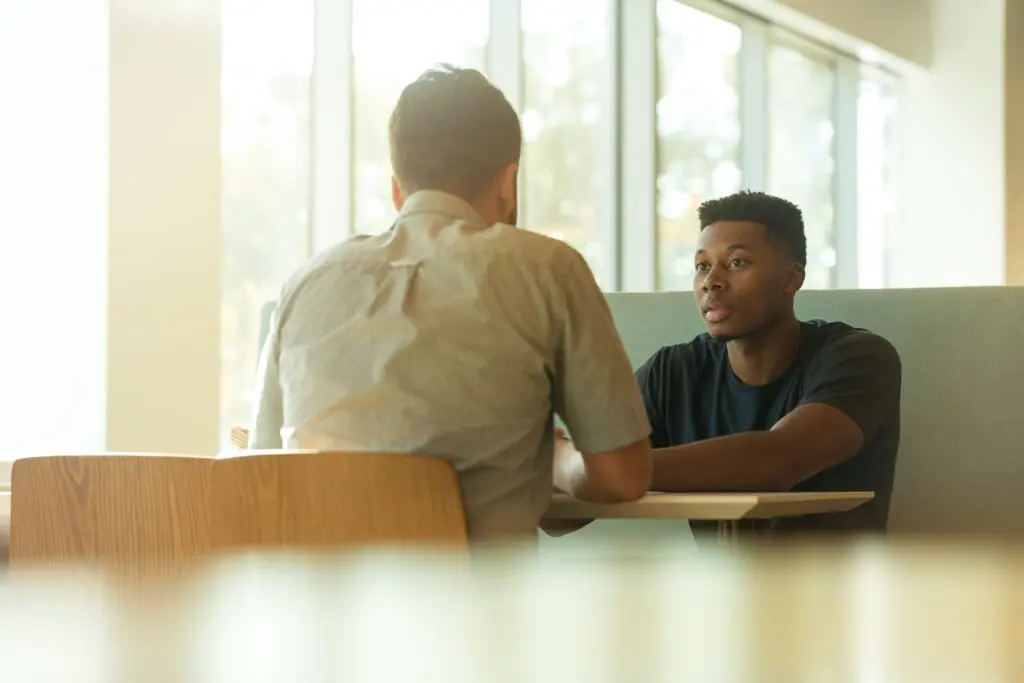 Student and adult sitting on wood table interacting with each other for support services